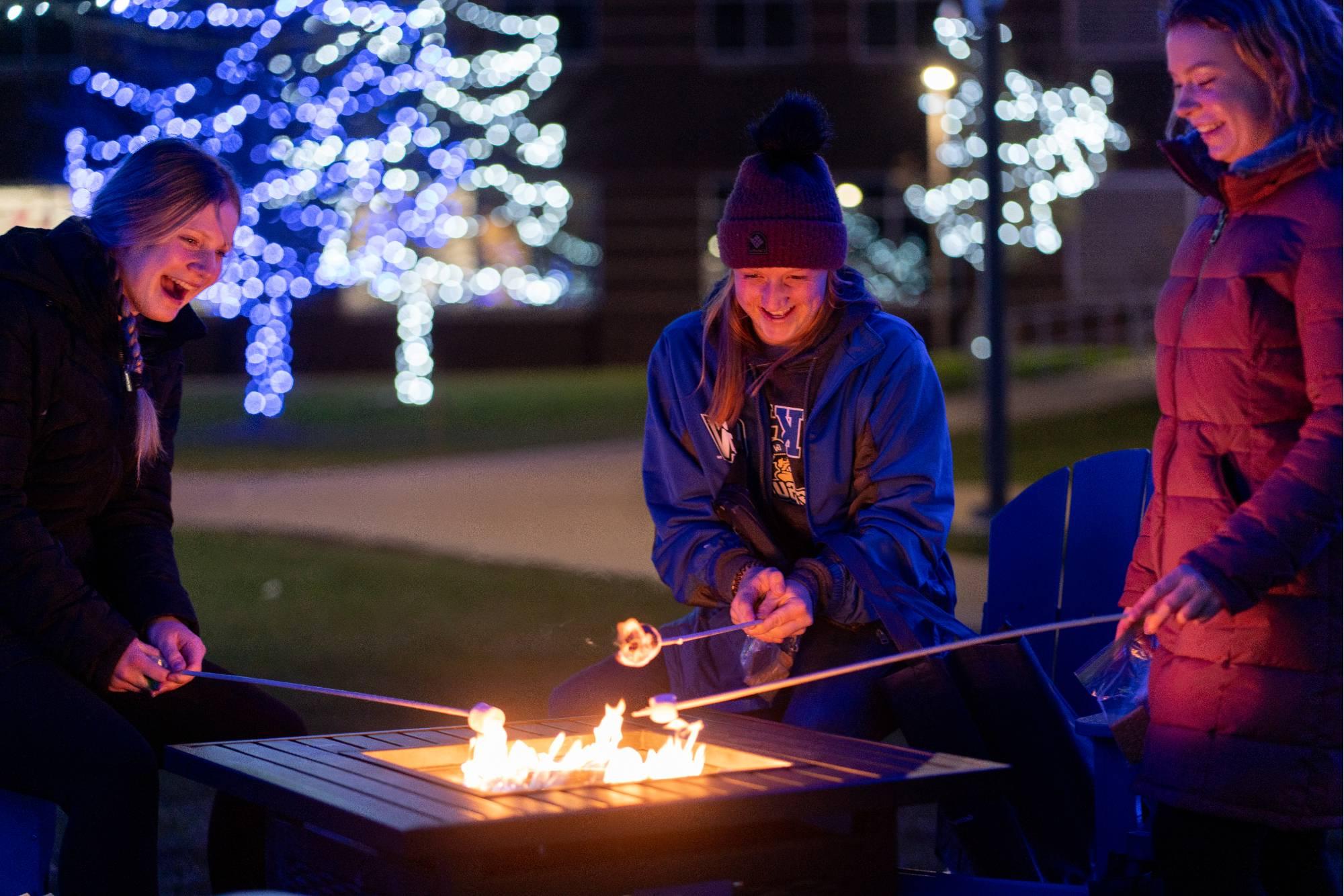 一群学生站在外面，围在篝火旁烤着s'mores.